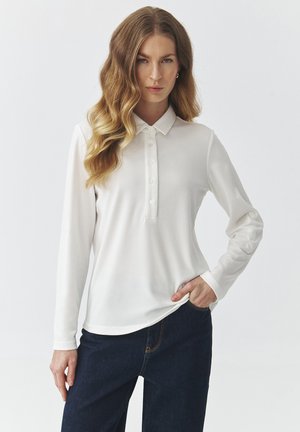 Polo shirt bianco a maniche lunghe con chiusura a bottoni e tessuto morbido e liscio. Presenta un colletto classico e maniche con polsini. Abbinato a jeans scuri.