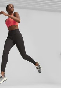 Un soutien-gorge de sport rose et un legging noir taille haute, tous deux en tissu extensible. Le soutien-gorge arbore un logo et les leggings ont des coutures latérales.