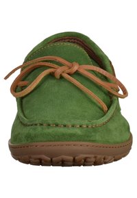 Chaussure mocassins en daim vert avec un bout arrondi, semelle en caoutchouc marron et lacets beige, présentant des coutures le long du bord.