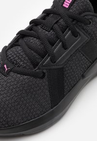 Zapatilla deportiva negra con parte superior de tela texturizada, acentos negros y marca en rosa. Cuenta con cierre de cordones y suela de goma para mayor agarre.