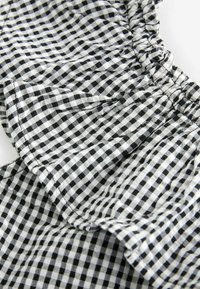 Czarnobiały materiał w kratkę w stylu gingham z falbaniastymi krawędziami, teksturowaną powierzchnią i marszczonymi detalami, tworzący warstwowy wygląd.