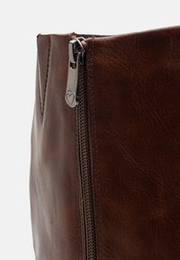 Brązowa skórzana torba z widocznym metalowym zamkiem błyskawicznym, z sercowym uchwytem. Tekstura jest gładka z delikatnym usłojeniem na powierzchni.