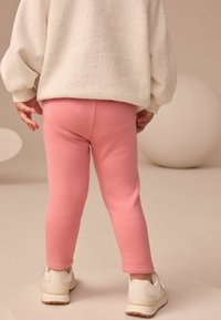 Różowe legginsy bawełniane o dopasowanym kroju, w połączeniu z jasnym, melanżowym swetrem i białymi trampkami. Prosty, casualowy wygląd.