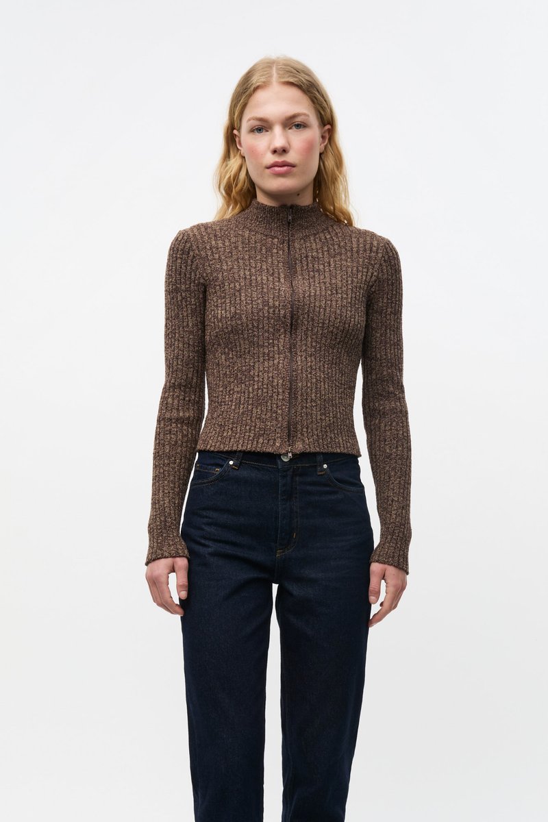 Ruskea ribbineulottu paita korkealla kauluksella ja täysipitkällä vetoketjulla, jossa pitkät hihat ja lyhyt malli, yhdistetty tummansinisiin korkeavyötäröisiin farkkuihin.