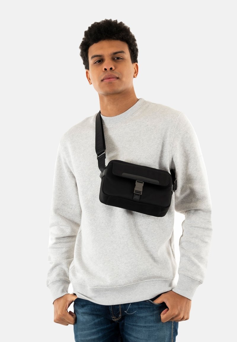 Borsa a spalla nera di forma rettangolare, con patta frontale e chiusura in metallo. Realizzata in tessuto liscio, presenta una tracolla regolabile.