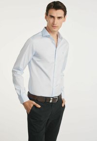 Jasnoniebieska koszula z długim rękawem wykonana z bawełny, z kołnierzykiem zapinanym na guziki, połączona z czarnymi spodniami i brązowym paskiem z ozdobnymi srebrnymi klamrami.