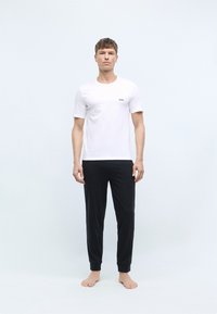 White short-sleeve t-shirt with a black logo on the chest, paired with black tapered jogger pants, displayed on a model in a plain background.