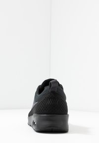 Sneaker Nike noir vu de l'arrière, montrant le talon perforé, la languette et le coussin d'air visible dans la semelle sur un fond blanc.