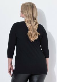 Černé tričko s tříčtvrtečními rukávy z hladké látky, s volným střihem a prodlouženým zadním lemem. Boční rozparek dodává jemný zajímavý detail.