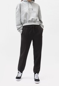 Felpa grigia accorciata con logo frontale, abbinata a pantaloni della tuta neri con polsini elasticizzati e vita con cordino. Sneakers nere completano il look.