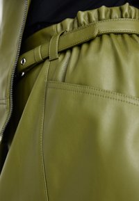 Olive green leather pants with a gathered waistband, adjustable belt, and visible stitching; smooth texture and structured design.