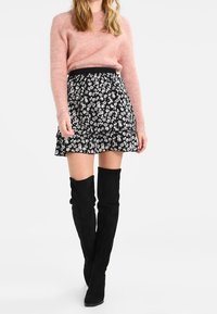 Suéter de punto rosa claro, minifalda negra con estampado floral y botas de ante negras por encima de la rodilla. Textura suave y patrones en contraste.