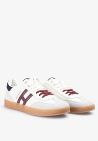 Zapatillas blancas con un diseño de franjas en color burdeos, detalles en el talón en azul marino, parte superior texturizada y suela de goma. Los cordones son burdeos, con la marca visible.