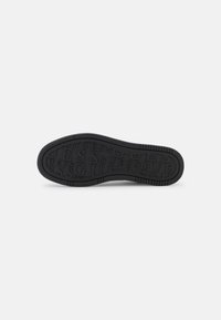 Suola di scarpa in gomma nera con grip testurizzato e motivo in rilievo con il logo "GUESS". Presenta bordi arrotondati e sezioni laterali rialzate per una maggiore aderenza.