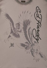 Camiseta de manga corta gris con grandes diseños de águila negra y gris y el texto "Ed Hardy". Material de algodón con un cuello redondo clásico.