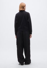 Abbinamento con felpa nera e pantaloni cargo, caratterizzato da una vestibilità rilassata, tessuto morbido e polsini elastici, con tasche sui pantaloni.