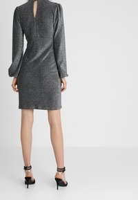 Kort silverglittrig klänning med långa ärmar och ett nyckelhål i ryggen. Matchad med svarta högklackade skor med genomskinliga remmar.