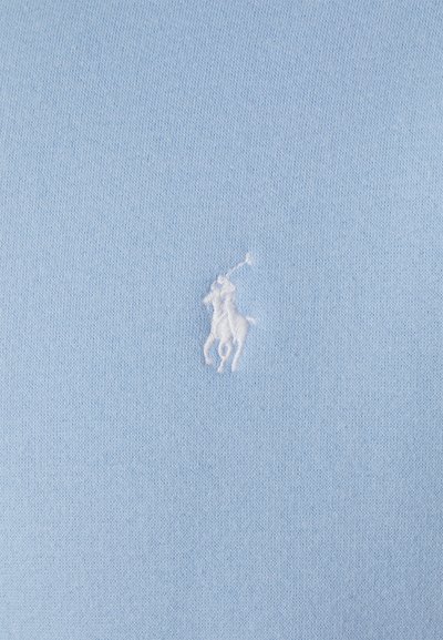 Tecido de algodão azul claro com um pequeno logótipo de jogador de polo bordado em branco no centro. A textura é lisa e uniforme.