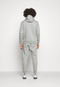 Grauer Hoodie und passendes Set aus Sweatpants, aus weichem Material mit elastischen Bündchen, ausgestattet mit Kapuze und minimalem Branding.