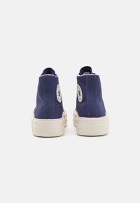 High-top sneakers made of navy canvas with white rubber soles. Features a circular brand patch on the outer sides.