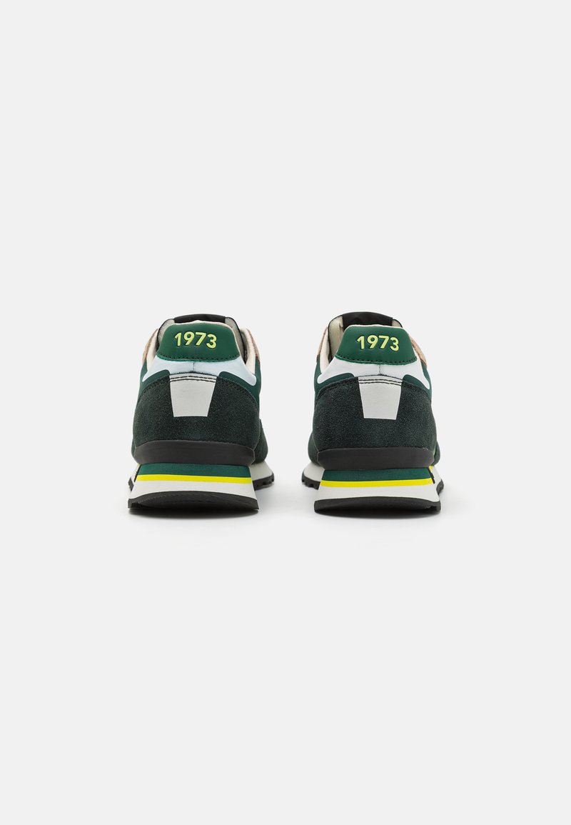 Zapatillas de ante verde con una suela de goma negra y blanca, con acentos amarillos y verdes, y el número "1973" en el talón.