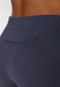 Sötétkék rugalmas leggings sima anyagból, magas derékkal; az "ONLY PLAY" logó a derékszegen van megmintázva.
