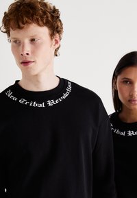 Sudaderas negras de manga larga, con el texto blanco "Neo Tribal Revolution" bordado en el cuello circular. Textura suave.