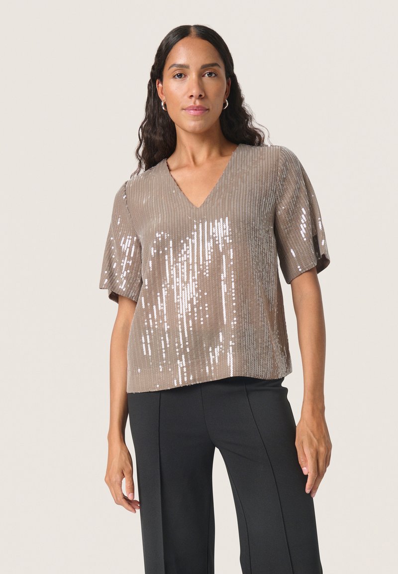 Kurzärmliges T-Shirt mit V-Ausschnitt in einem hellbraunen Farbton, das eine strukturierte Oberfläche mit kleinen Pailletten aufweist, die das Licht reflektieren.