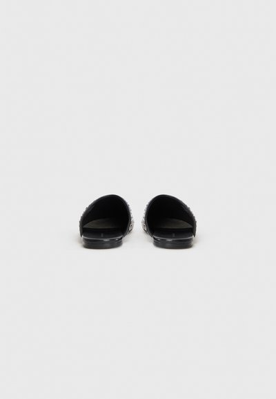 Des sandales noires à glissière avec un arrière ouvert, en matériau lisse imitant le cuir, ornées d'éléments en argent sur les côtés et dotées de semelles plates.