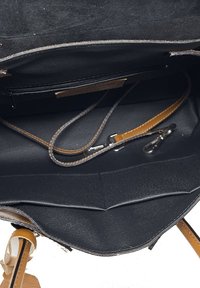 Wnętrze czarnej skórzanej torebki z kieszonką na zamek, dwoma przegródkami i odpinanym brązowym paskiem. Gładka tekstura i minimalna ilość detali metalowych.