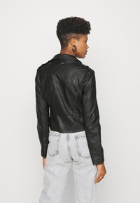 Schwarze Leder-Cropped-Jacke mit taillierter Passform, Schulterklappen und glatter Textur, kombiniert mit hellgrauen Jeans.