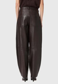 Brūnas ādas platmala bikses ar aizmugurējām kabatām un redzamām diega detaļām. Gluda tekstūra ar pielāgotu dizainu un augstu jostu.