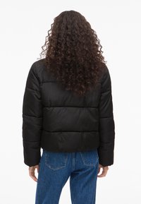 Čierna prešívaná bunda s krátkym strihom, prešívanou textúrou a dlhými rukávmi. Kombinovaná s modrými rifľami s detailom zadného vrecka.