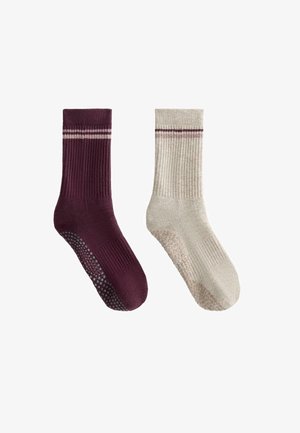 Két pár zokni: az egyik sötét burgundi színű, bordázott textúrával és csúszásmentes talppal, a másik világos bézs színű, finom függőleges csíkokkal.