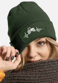 Dark green knitted beanie featuring a rectangular patch with a white tractor and heartbeat line design. Soft texture with ribbed detail.