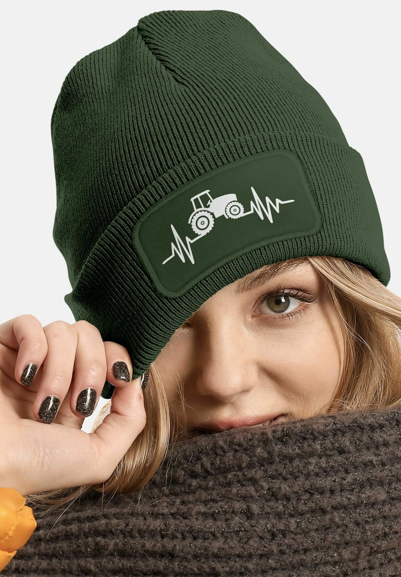 Dark green knitted beanie featuring a rectangular patch with a white tractor and heartbeat line design. Soft texture with ribbed detail.