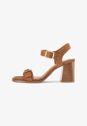 Brązowa sandałka z zamszu z odkrytymi palcami, klockowym obcasem, paskiem wokół kostki i złotymi sprzączkami, o minimalistycznym designie i obcasie o fakturze drewna.
