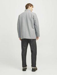 Grau melierter Wollmixmantel mit einem hohen Kragen, schlankem Design, geradem Schnitt und dunklen Jeans. Verfügt über eine Hinternaht. Schwarze Schuhe mit dicken Sohlen.