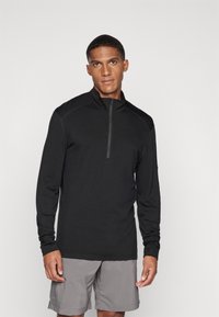 Pullover preto de mangas longas com gola de fecho de quarto, feito de material leve, combinado com calções cinzentos. Textura suave, design ajustado.
