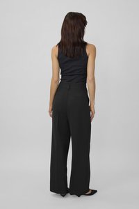 Black wide-leg trousers with faux pockets and a smooth texture, paired with a fitted black tank top. Visible seams at the waist.