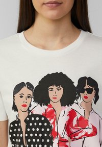 T-shirt en coton blanc avec une illustration graphique de trois femmes. L'une porte un haut à pois, une autre a des cheveux frisés, et la dernière porte des lunettes de soleil.