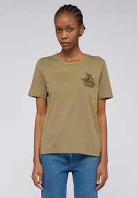 Olivgrünes T-Shirt mit kurzen Ärmeln aus weicher Baumwolle, das auf der Vorderseite über strukturierte diagonale Linien und ein gesticktes Logo auf der Brust verfügt.