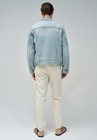 Hellblaue Jeansjacke mit lockerer Passform, ausgestattet mit einem spitzen Kragen, Seitentaschen und Knopfverschlüssen. Kombiniert mit beigen Hosen.