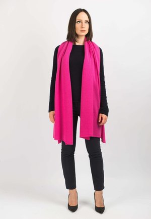 Sciarpa fucsia realizzata in tessuto morbido, che si drappeggia in modo elegante. Indossata sopra una maglietta nera e pantaloni neri, abbinata a tacchi a punta neri.