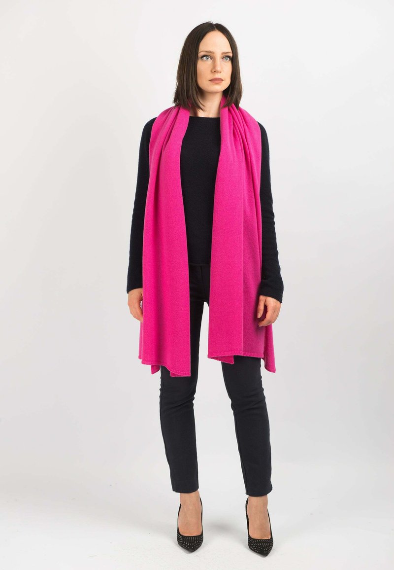 Fuchsia tørklæde lavet af blødt stof, der hænger elegant. Båret over en sort top og sorte bukser, parret med sorte spidse hæle.