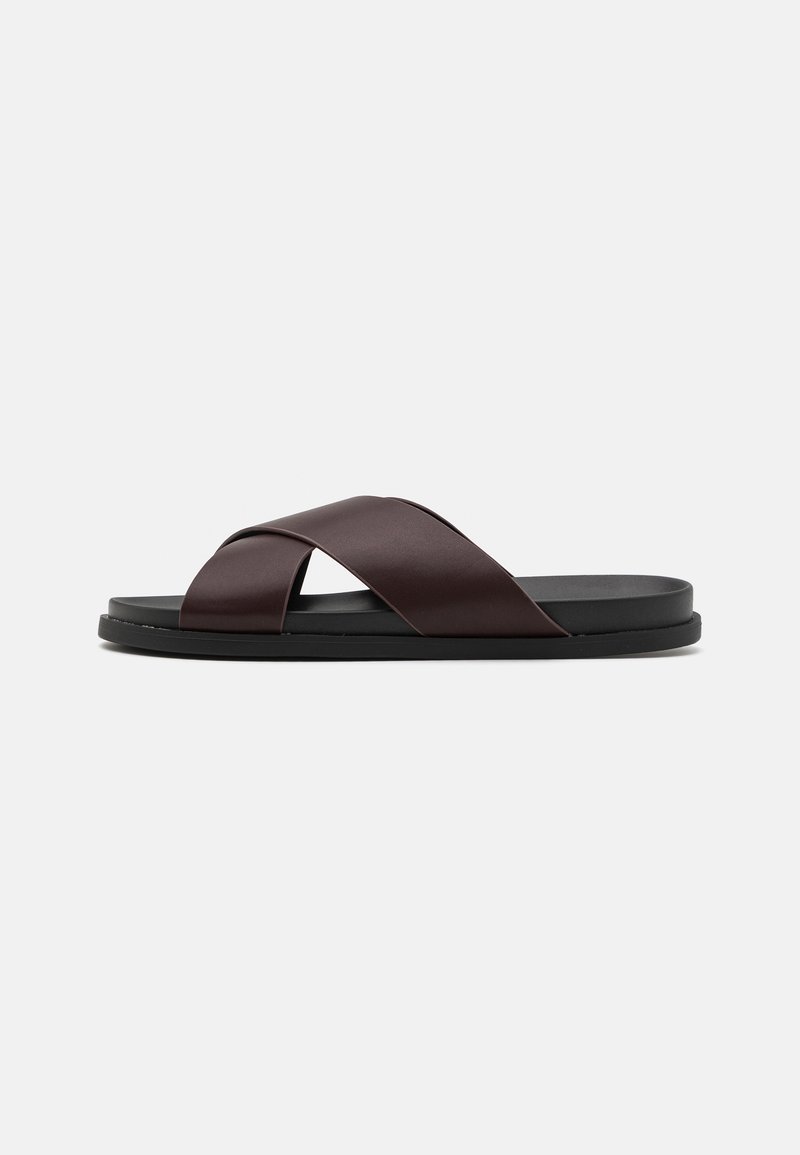Sandales en cuir marron pour homme avec deux larges brides croisées et une semelle plate noire sur un fond clair uni.