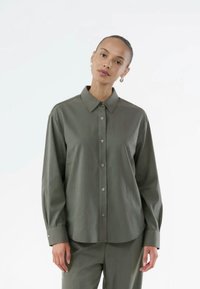 Chemise boutonnée vert olive à coupe décontractée, avec un col classique, des manches longues et des boutons argentés le long de la patte de boutonnage et des poignets.