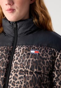 Pufferjakke med leopardmønster i brunt og svart, med en glanset svart krage og en Tommy Jeans-logo på brystet.