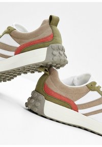Baskets de sport en vert olive, beige et blanc avec une semelle texturée. Présente une bande d'accent rouge et une languette au talon.