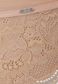 Nacktes Spitzengewebe mit floralen Mustern und zarten Verzierungen. Verfügt über eine glatte Textur und eine schlanke Linie mit einem metallischen Verschluss.